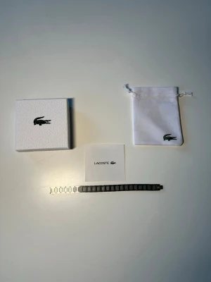 Lacoste Armband - Lacoste armband i silverfärg. Stilren och modern design, passar till allt. I fint skick och kommer med originalask. Snabb leverans 🚚 