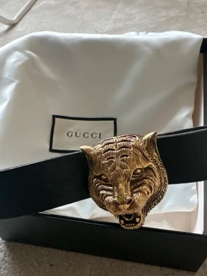Gucci bälte med tiger(feline) huvud - Väldigt bra skick. Herrbälte från Gucci. Köpt för 5000kr. Svart läderbälte med guldfärgad tungt huvud. Köpt 2018, bra bevarat. Kommer med sin låda och påse. Säljs då det används sällan. Finns plats på läderbältet att göra egna hål ifall det inte skulle passa. Säg gärna till om ni vill ha fler bilder! Slutsåld på deras hemsida. Storlek 85cm.