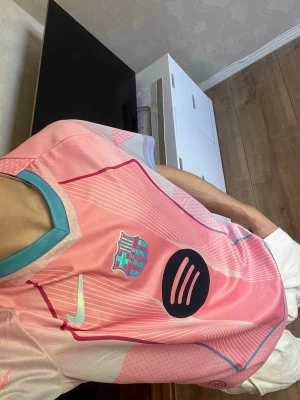 Rosa FC Barcelona matchtröja Nike - Snygg rosa FC Barcelona matchtröja från Nike med turkosa detaljer och klubbmärke på bröstet. Tröjan har svart Spotify-logga framtill, Champions League-märke på ärmen och är tillverkad i lätt, ventilerande material. Perfekt för fotbollsträning eller att bära som supporter. Helt ny, så inga defekter eller liknande, lappen kvar som syns på bilderna (medföljer lappen som är på). Om du har några frågor, tveka inte på att höra av dig😊