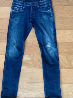 Blå Replay jeans med slitningar - Snygga blå jeans från Replay med klassisk femficksmodell och slitna detaljer på knäna. Jeansen har raka ben och tydliga kontrastsömmar samt logga på bakfickan. Perfekta för en avslappnad och trendig look.