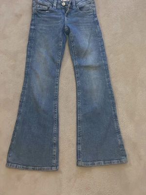 Blå bootcut jeans med detaljerade fickor - Säljer ett par blå bootcut jeans med snygg tvätt och designade bakfickor med knappar. Jeansen har klassisk modell. 