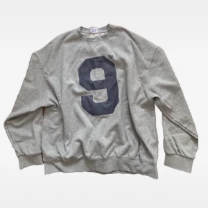Grå sweatshirt - Cool grå sweatshirt med en stor svart siffra 9 tryckt på framsidan. Tröjan har rund hals, långa ärmar och ribbade muddar vid ärmslut och nederkant. Perfekt för en avslappnad streetstyle-look.