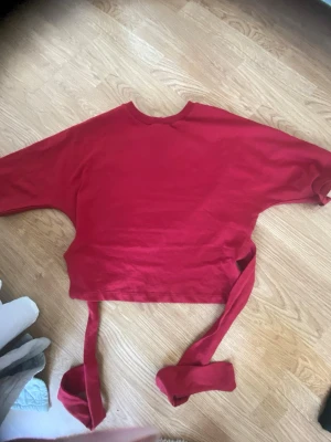 Röd croppad tröja med knytband - Trendig röd croppad tröja med långa ärmar och breda knytband i midjan. Perfekt för att skapa en cool och avslappnad look. Rund halsringning och mjukt material som känns skönt mot huden.