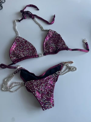 Tävlingsbikini bikinifitness  - Superfin tävlingsbikini färgen Rasberry med jätte fina kristall stenar som skiftar i olika färger. Överdelen har trekantsform och knyts i nacken och ryggen med pärlband. Underdelen har pärlband i sidorna och matchande strassdetaljer. Perfekt för dig som vill sticka ut på bikinifitness scenen tog hem guldet i denna bikinin 😍. Jag är 161cm lång och vägde 53-54kg  på scenen 