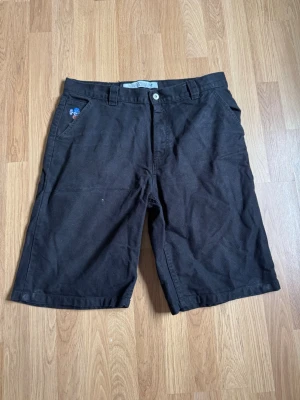 Svarta shorts från Polar - Säljer ett par svarta shorts från Polar med klassisk design och raka ben. Shortsens material är bomull och de har både fram- och bakfickor samt bälteshällor. En liten Polar-logga finns på fickan och en gul patch på baksidan. Perfekta för sommaren!