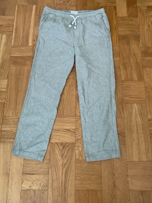Grå linnebyxor från Jack & Jones - Snygga grå linnebyxor från Jack & Jones med avslappnad passform och dragsko i midjan. Byxorna har sidfickor och är tillverkade i ett lätt och luftigt linnematerial. Knappt använda.