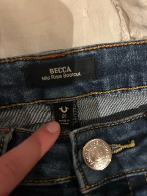True Religion bootcut jeans blå - Snygga blå bootcut jeans från True Religion, modell BECCA Mid Rise Bootcut. Jeansen har klassisk femficksdesign, orange kontrastsömmar och silverfärgad knapp. Perfekt passform med medelhög midja och utsvängda ben.❣️❤️(deras pris är 1300kr❣️)