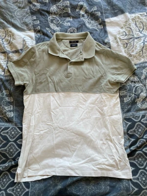 Grön och vit pikétröja från Massimo Dutti - Snygg pikétröja tvåfärgad design med ljusgrön överdel och vit nederdel. Tröjan har klassisk krage, korta ärmar och knäppning framtill. Perfekt för en avslappnad och stilren look.