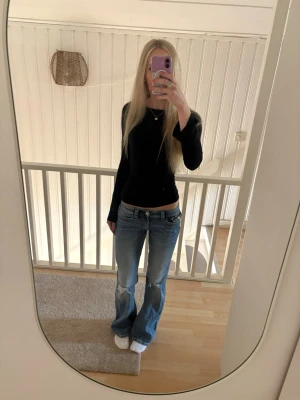 Blå bootcut jeans med broderade fickor - Säljer ett par blå bootcut jeans från Gina tricot young med snygga röda broderier på bakfickorna. Jeansen har låg midja, klassisk femficksdesign och är tillverkade i denim med lätt slitning framtill. Perfekta för en avslappnad och trendig look.
