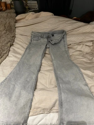Grå utsvängda jeans från Divided - Säljer ett par gråa utsvängda jeans från Divided. Jeansen har hög midja, klassisk femficksmodell och vida ben som ger en retroinspirerad look. Perfekta för dig som gillar en avslappnad men trendig stil.