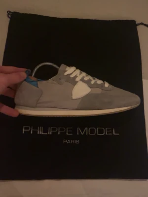 Grå Philippe Model skor - Snygga sneakers från Philippe Model i grå mocka med vita detaljer och vit sula. Skorna har en låg siluett, vita skosnören och en blå detalj vid hälen. Perfekta för dig som gillar stilrena och trendiga sneakers.storlek 40