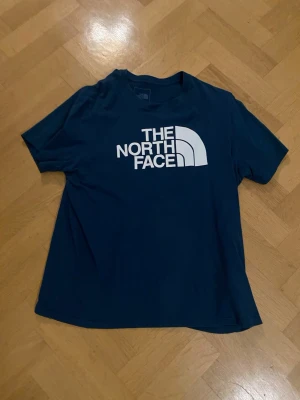 Blå t-shirt från The North Face - Säljer en blå t-shirt från The North Face med stort vitt logotryck på bröstet. 