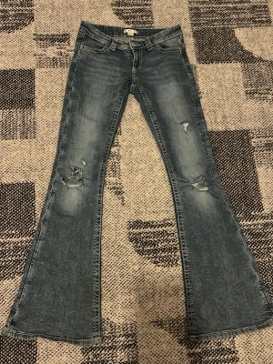 Blå bootcut jeans med slitningar - Säljer ett par jättefina blå bootcut jeans med slitningar på knäna och snygga broderade bakfickor. storlek xs 14+ från gina! endast använd några gånger💓