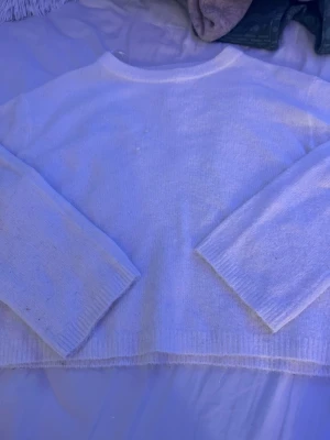 Vit stickad tröja med rund hals - En enkel och stilren vit stickad tröja med rund halsringning och långa ärmar. Tröjan har ribbstickade muddar vid ärmslut och nederkant. Perfekt för lager-på-lager och passar till det mesta.