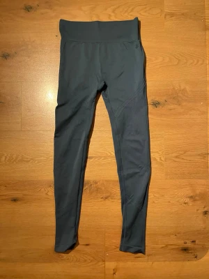 Mörkgrå seamless leggings - Snygga mörkgrå seamless leggings med hög midja och ribbad linning. Materialet är stretchigt och följsamt, perfekt för träning eller chill. Diskret logga vid höften och coola detaljer längs benen för extra stil.