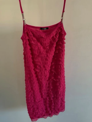 Rosa volangklänning från D&G - Säljer en rosa kortklänning från D&G med tunna axelband och volangdetaljer över hela klänningen. Klänningen har en figurnära passform och är perfekt för sommarens alla tillfällen. Materialet känns lätt och luftigt.