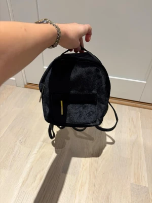 Svart Björn Borg miniryggsäck med dragkedja som NY - En liten och stilren svart ryggsäck med dragkedja framtill och justerbara axelband. Väskan har en enkel design och är gjord i syntetmaterial med en matt finish. Perfekt för dig som vill ha en smidig och snygg accessoar till vardagen.använd 1 gång från björn borg