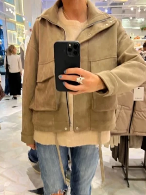 Beige mockajacka med fickor - Snygg beige mockajacka med stora fickor framtill och dragkedja. Jackan har en loose passform och långa ärmar. Perfekt för dig som gillar en avslappnad men trendig stil.