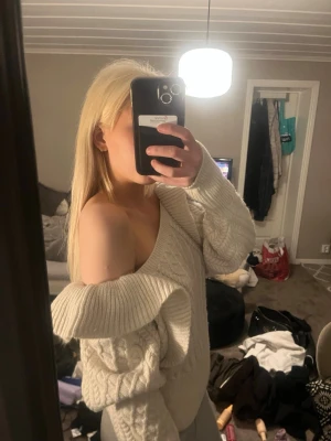 Vit off-shoulder stickad tröja - Säljer en vit stickad tröja med off-shoulder design och breda ärmar. Tröjan har ett snyggt kabelstickat mönster framtill och ribbade muddar. Perfekt för dig som gillar en avslappnad och trendig look.