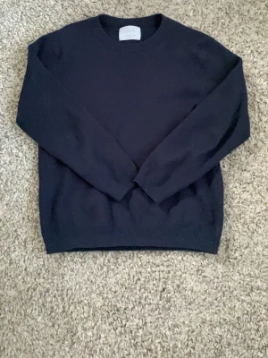 Mörkblå stickad tröja från Zara - En stilren mörkblå stickad tröja från Zara med rund halsringning och långa ärmar. Tröjan har en klassisk, rak passform och är perfekt för lager-på-lager. Enkel design utan mönster, vilket gör den lätt att matcha med olika outfits.