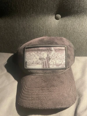 Svart keps med fototryck av Zlatan Ibrahimović - Säljer en svart keps i velvet med ett stort fototryck framtill som visar en fotbollsspelare som firar på en arena. Kepsen har böjd skärm och justerbar baksida. Perfekt för dig som gillar sportig och unik stil.