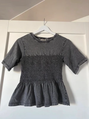 Grå topp med smock och volang -  grå topp med smockad midja och volang nedtill. Aldrig använd! 