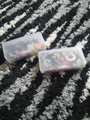 Två askar med färgglada bokstavspärlor - Säljer två genomskinliga plastaskar fyllda med färgglada bokstavspärlor i olika mönster och färger. Perfekt för pyssel, smyckestillverkning eller dekoration. Askarna är smidiga att ta med och håller pärlorna organiserade.