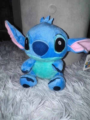 Stitch gosedjur från Disney 20cm - Supergulligt Stitch gosedjur ca 20cm från Disney i blått och turkost med stora öron och svarta detaljer. Mjuk och kramvänlig, perfekt för alla som älskar Lilo & Stitch. Tillverkad i plyschmaterial och har broderade ögon och detaljer.