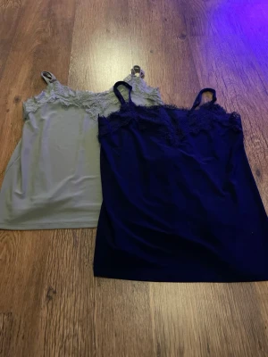 Två spetskantade nattlinnen - Säljer två nattlinnen med tunna axelband och spetsdetaljer vid urringningen. Ett är ljusgrönt och det andra är mörkblått. Båda har en mjuk och följsam känsla, perfekta för att chilla hemma eller sova i. Materialet känns lent mot huden och ger en avslappnad vibe.