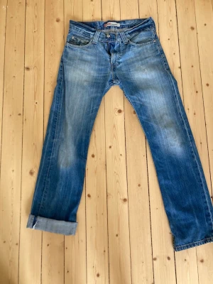Levi's blå raka jeans - Klassiska blå jeans från Levi's med raka ben och fem fickor. Jeansen har en snygg tvättad look med slitningar på låren och knäna samt uppvikta benslut. Tillverkade i bomull med en autentisk denimkänsla. Perfekta för en avslappnad streetstil.