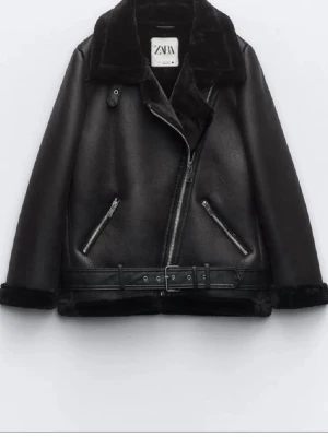 Svart pälsjacka från Zara - Säljer en svart pälsjacka från Zara med bred krage, dragkedja i sned modell och två snedställda fickor med dragkedja. Jackan har bälte i midjan och mjukt foder. Perfekt för kalla vinterdagar och riktigt snygg till alla outfits.