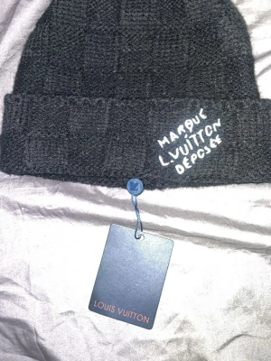 Svart   mössa - Snygg svart mössa från  med diskret rutmönste och broderad vit text ' framtill. Mössan är stickad och har en klassisk uppvikt kant. Perfekt accessoar för att lyfta din streetstyle. Helt ny oanvänd ✅