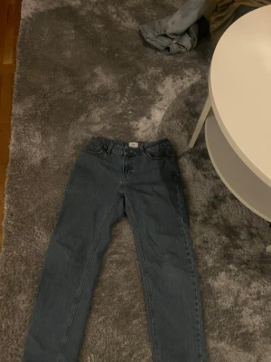 Blå raka jeans med hög midja - Säljer ett par klassiska blå jeans med rak passform och hög midja. Jeansen har fem fickor och breda benslut, perfekta för en avslappnad och trendig look. Tillverkade i denim med en snygg tvättad finish.