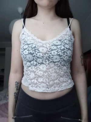 Vit spetsig croppad linnetopp - Säljer en vit croppad linnetopp med tunna axelband och v-ringning. Toppen är helt i spets med blommigt mönster och har en lätt transparent look. Perfekt för lager-på-lager eller som statement-piece till din outfit.