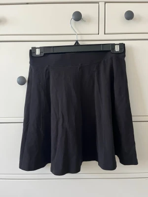 Svart kortkjol  - Enkel och stilren svart kortkjol med lätt utställd passform. Kjolen är sydd i mjuk bomull och har en bred midjeresår. Storlek 158/164 men passar XS/S.