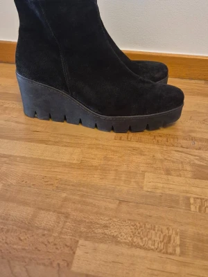 Svarta kilklackade stövletter i mocka - Snygga svarta stövletter i mocka med kilklack och grov sula. Dragkedja på sidan för enkel på- och avtagning. Finns att köpa online för runt 1700 kr som högst(sista bilden).Perfekta för dig som vill ha både höjd och komfort i ett par boots😜🌸 (storlek mellan 40 och 40 1/2)