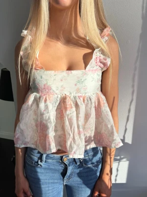 Blommig volangblus - Söt blommig blus i ljusa toner med volangdetaljer på axlarna och öppen rygg med knytband. Passar även S.