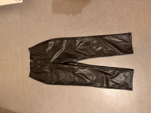 Byxor i konstläder - Fina byxor i konstskinn. De är raka i modellen, dock har de legat ihopvikta länge i min garderob så de ser skrynkliga ut. Finns några mindre skavanker som synes på bild, men det är inget som stör när man har på sig dem. Modellen heter Bianca. Det finns en dold dragkedja på sidan av byxorna.