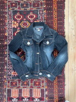 Mörkblå jeansjacka - Snygg mörkblå jeansjacka med vita vertikala ränder och stora silverfärgade knappar. Jackan har klassisk krage, två bröstfickor med lock och långärmad design. Perfekt för dig som gillar en cool och tidlös look.