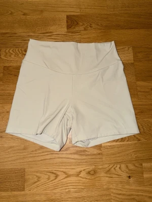 Vita högmidjade shorts från Oysho - Säljer ett par vita högmidjade shorts från Oysho Sport. De är tillverkade i ett stretchigt syntetmaterial som passar perfekt för träning. Shortsen har en clean design utan synliga detaljer och sitter tight mot kroppen.