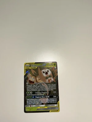 Pokémonkort Rowlet & Alolan Exeggutor GX - Säljer ett Pokémonkort med motiv av Rowlet & Alolan Exeggutor GX. Kortet har färger i grönt, brunt och gult med glansig yta och TAG TEAM-design. Text och illustration på framsidan. Perfekt för samlare eller Pokémonfans.
