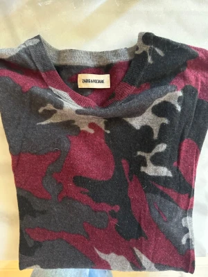 Camo-mönstrad Kashmir tröja Zadig & Voltaire - Stickad tröja från Zadig & Voltaire i snyggt camouflage-mönster i rött, svart och grått. En cool och lite mer edgy modell som samtidigt är lätt att matcha.  Tunn och mjuk stickning som gör den perfekt att bära året runt.  Storlek: M/L men passar även S beroende på hur man vill att den sitter (oversized). Skick: Superfint skick, inga hål eller fläckar. Nypris: ca 3 900 kr.