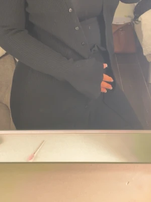 Lång svart stickad kofta - Säljer en lång, svart stickad kofta med knappar framtill. Koftan har ribbade ärmar och en rak passform som ger en clean look. Perfekt att slänga över en outfit för extra lager och stil.