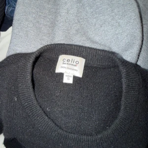 Svart cashmere-tröja från Celio - Mjuk och stilren svart stickad tröja från Celio i 100% cashmere. Tröjan har rund halsringning, långa ärmar och ribbade muddar vid ärmslut och nederkant. Perfekt för en klassisk och enkel look.