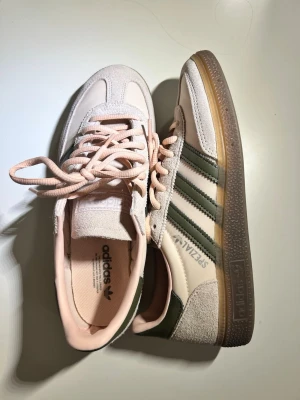 Adidas Spezial sneakers beige/grön - Snygga Adidas Spezial sneakers i beige mocka med gröna läderdetaljer och klassiska tre ränder på sidan. Skorna har gummisula och ljusrosa snören samt innerfoder. Perfekta för dig som gillar retrovibbar och streetstyle.
