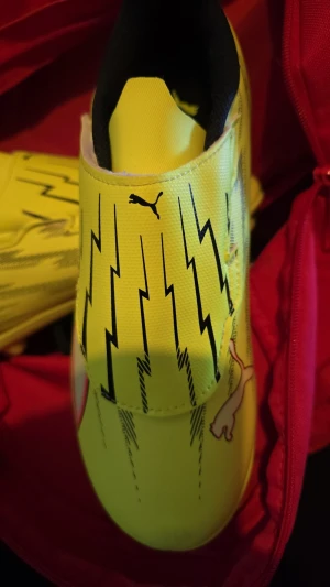 Puma gula fotbollsskor med blixtmönster - PUMA Ultra 6 Match Laceless + MG Unleashed. STORLEK EU 36.                                                     Snygga gula fotbollsskor från Puma med svart blixtmönster och klassisk logga. Skorna har dobbar för bra grepp på planen och en slimmad, modern form.  Perfekta för dig som vill sticka ut på matchen!