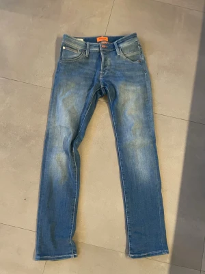 Ljusblå slim jeans  - Säljer ett par blå jeans med slim. Klassisk femficksmodell med knapp och dragkedja. Jeansen har en avslappnad tvättad look och passar perfekt till en casual stil. Materialet är denim i bomull.  Jack Jones storlek 28/30