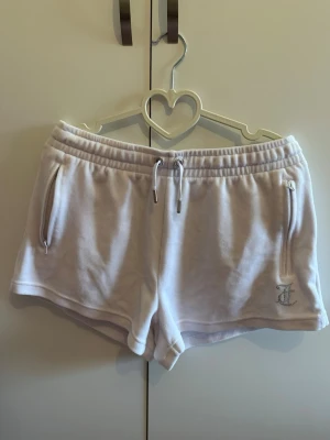 Vita Juicy Couture shorts - Superfina vita shorts från Juicy Couture med strassdetaljer och logga på ena benet. Shorts med snörning i midjan och dragkedjefickor. Perfekta för sommaren och riktigt sköna att ha på sig.