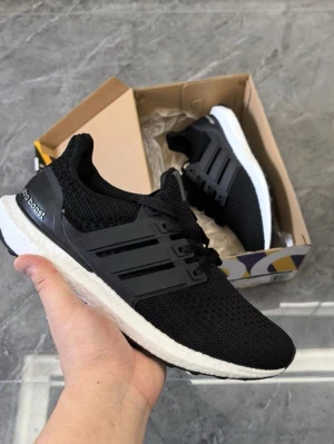 Svarta Adidas Ultra Boost sneakers - Svarta Adidas Ultra Boost sneakers med stickad ovandel, svarta plastdetaljer och vit Boost-sula. Klassisk tre-randig design på sidorna och svart hälkappa med Ultra Boost-logga. Perfekta för en sportig och stilren look.