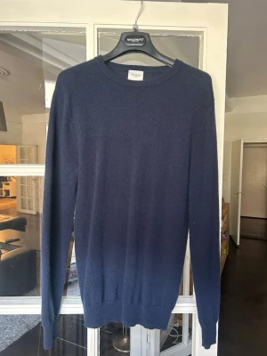 Mörkblå stickad tröja John Henric  - Mysig mörkblå stickad tröja från John Henric i klassisk modell med rund hals och långa ärmar. Tillverkad i mjukt material som känns lyxigt och passar perfekt till många olika stilar. Ribbstickade muddar vid ärmslut och nederkant.